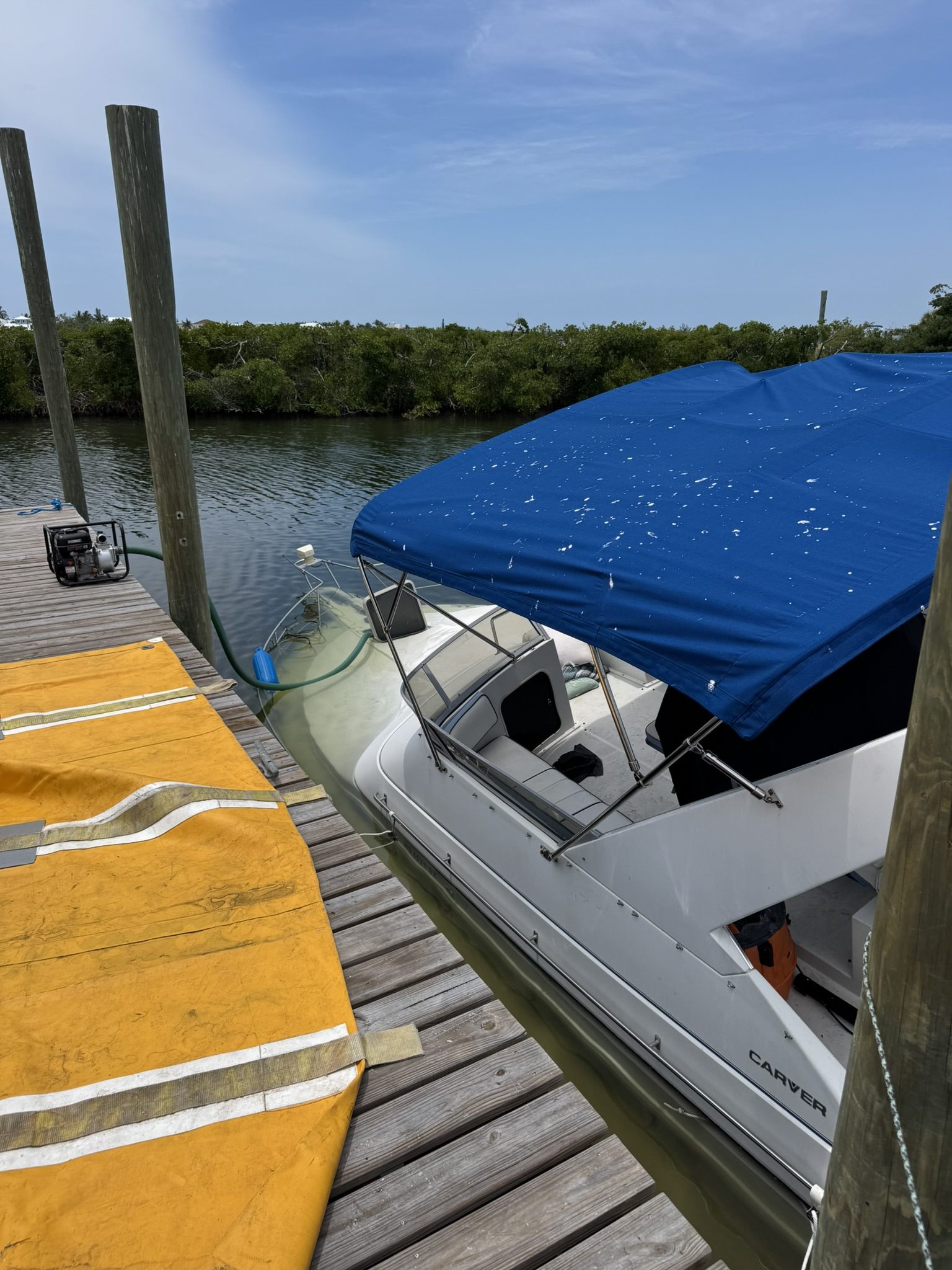 Recovery pump and hose setup beside a partially submerged boat in a canal