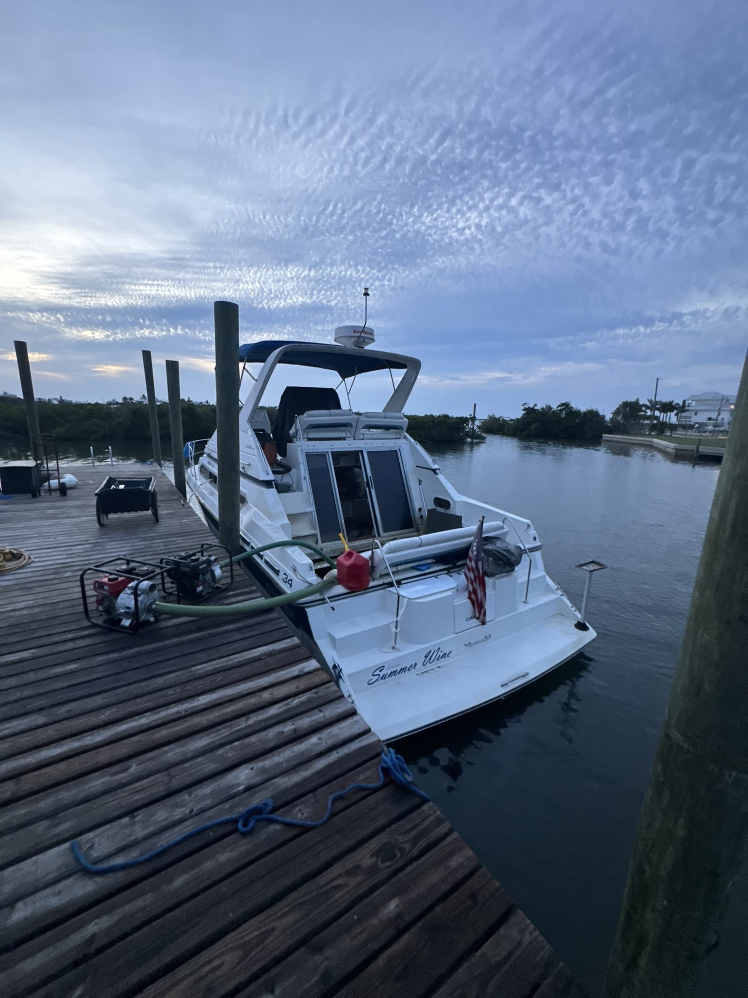 Boat recovery crew staging pumps and hoses at dusk beside a flooded cabin cruiser